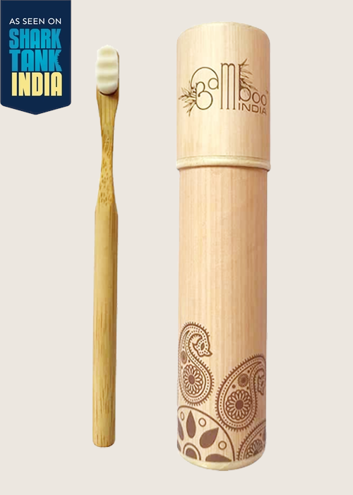 Bamboo toothbrush with a round handle, displayed alongside its cylindrical packaging with floral patterns. The packaging is labeled with 'Bamboo India' and has a paper box visible in the background.